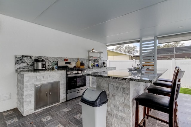 kitchen with dark stone countertops, a kitchen breakfast bar, a healthy amount of sunlight, and gas range