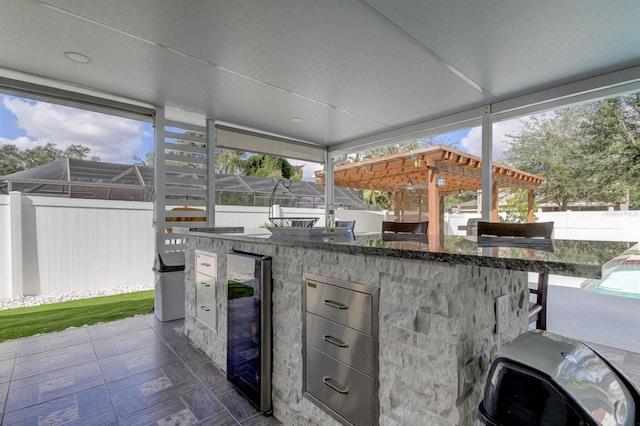 view of patio / terrace featuring exterior kitchen, a fenced backyard, outdoor wet bar, wine cooler, and a pergola
