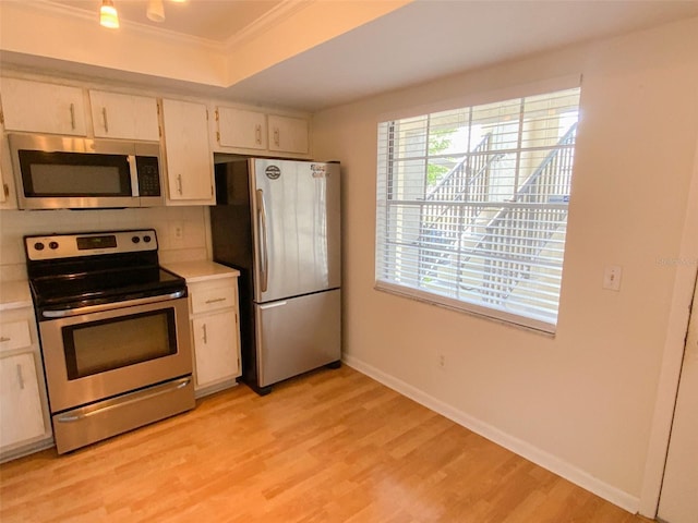kitchen featuring crown molding, baseboards, light countertops, light wood finished floors, and stainless steel appliances