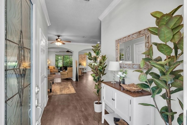 foyer entrance featuring ornamental molding, ceiling fan, arched walkways, and dark wood-type flooring