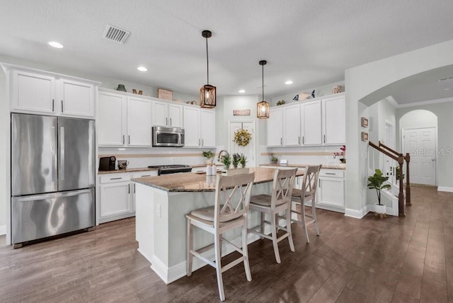 kitchen featuring appliances with stainless steel finishes, arched walkways, white cabinetry, dark wood finished floors, and recessed lighting