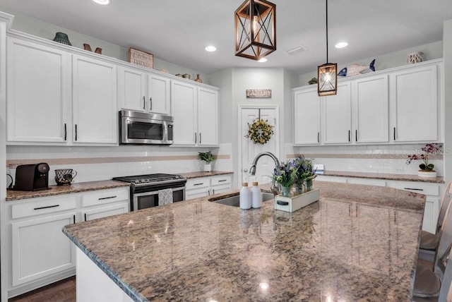 kitchen featuring appliances with stainless steel finishes, a sink, a center island with sink, white cabinets, and stone counters