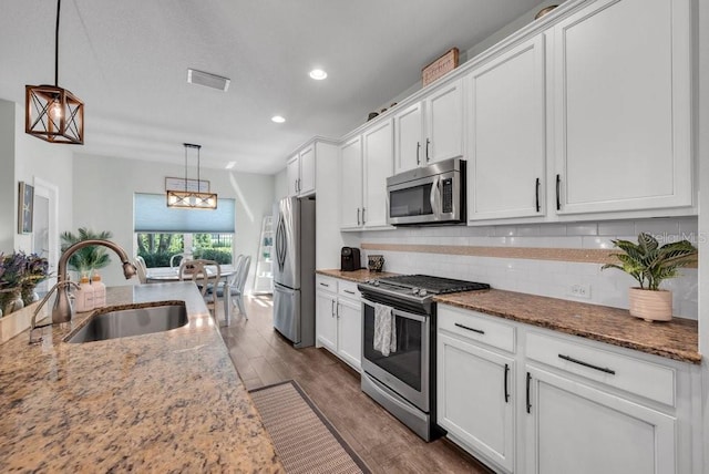 kitchen featuring appliances with stainless steel finishes, a sink, white cabinets, dark wood-style floors, and decorative backsplash