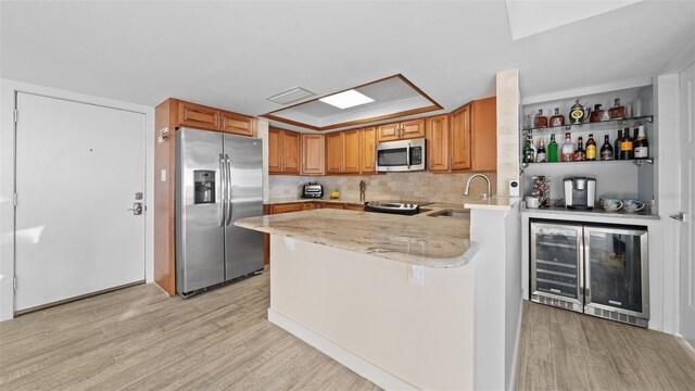 kitchen featuring appliances with stainless steel finishes, a sink, light wood finished floors, and wine cooler