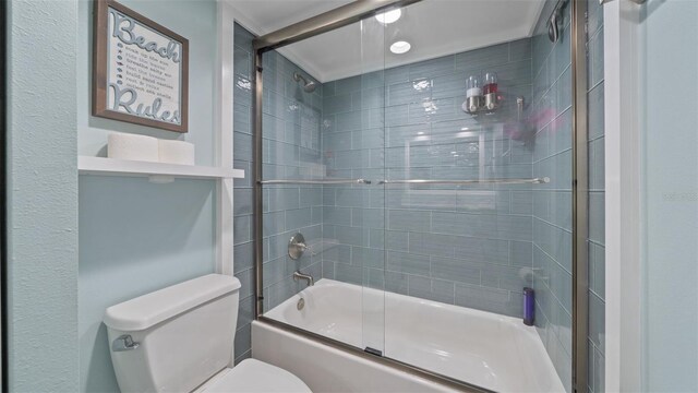 bathroom featuring toilet and shower / bath combination with glass door
