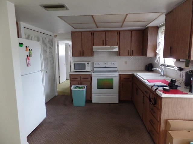kitchen with a sink, light countertops, under cabinet range hood, white appliances, and dark carpet