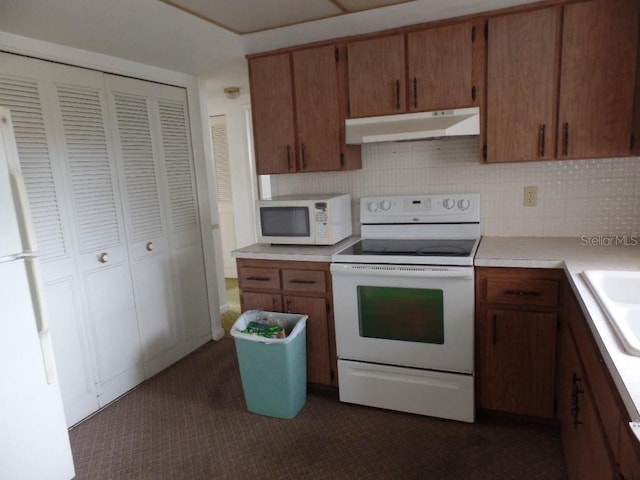 kitchen featuring white appliances, dark colored carpet, light countertops, under cabinet range hood, and brown cabinets