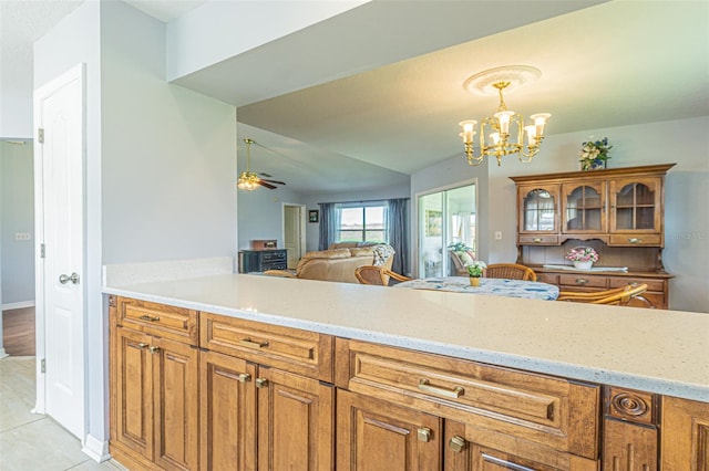 11311 Corey Pavin Ln, San Antonio, FL 33576 - kitchen with brown cabinets, a chandelier, a ceiling fan, light tile patterned flooring, and light stone counters