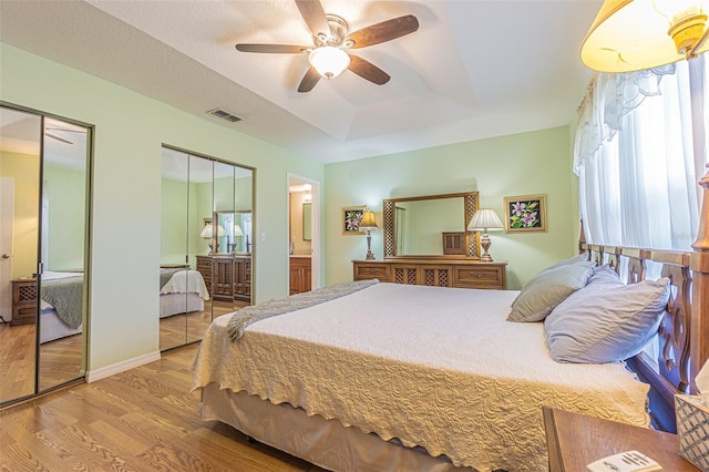 11311 Corey Pavin Ln, San Antonio, FL 33576 - bedroom featuring two closets, wood finished floors, a raised ceiling, ceiling fan, and ensuite bath