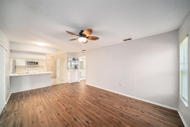 unfurnished living room with ceiling fan, a textured ceiling, visible vents, wood finished floors, and baseboards