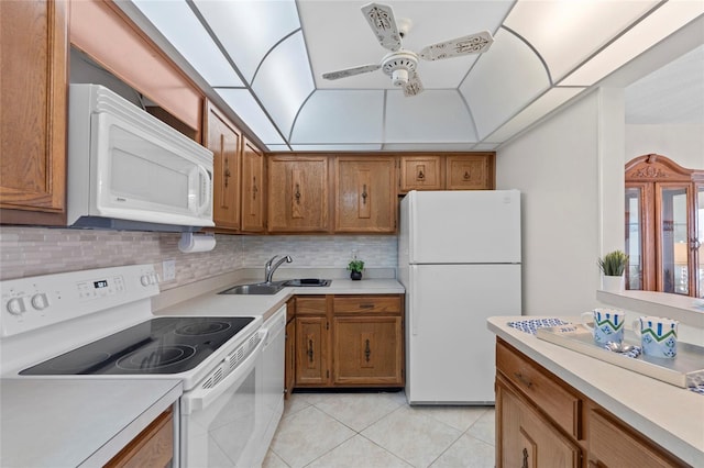 kitchen with a sink, white appliances, brown cabinets, light countertops, and light tile patterned floors
