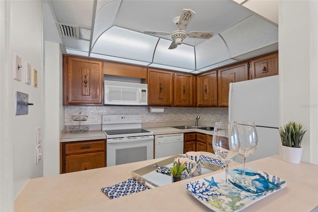 kitchen featuring brown cabinetry, white appliances, visible vents, backsplash, and light countertops