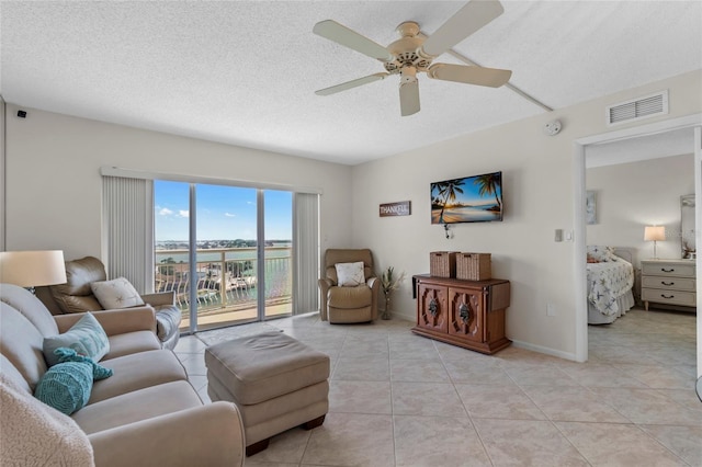 living room featuring a textured ceiling, visible vents, a ceiling fan, light tile patterned floors, and baseboards