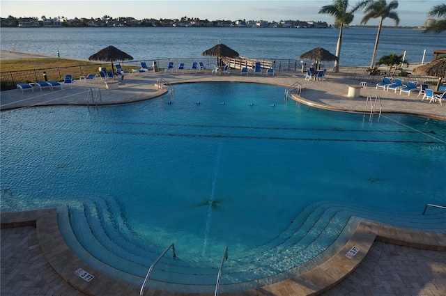 community pool featuring fence, a water view, and a patio area