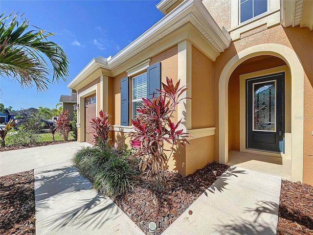 property entrance with a garage, stucco siding, and driveway