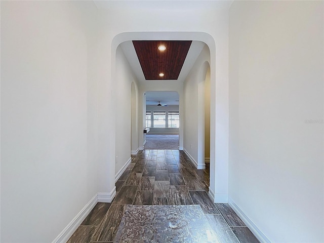 hall featuring baseboards, arched walkways, wood finished floors, and recessed lighting