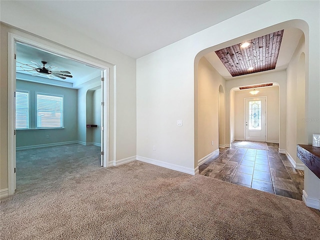 carpeted foyer entrance featuring arched walkways, baseboards, and a ceiling fan