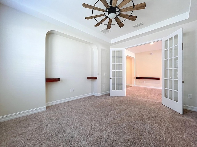 carpeted spare room featuring a ceiling fan, french doors, visible vents, arched walkways, and a raised ceiling