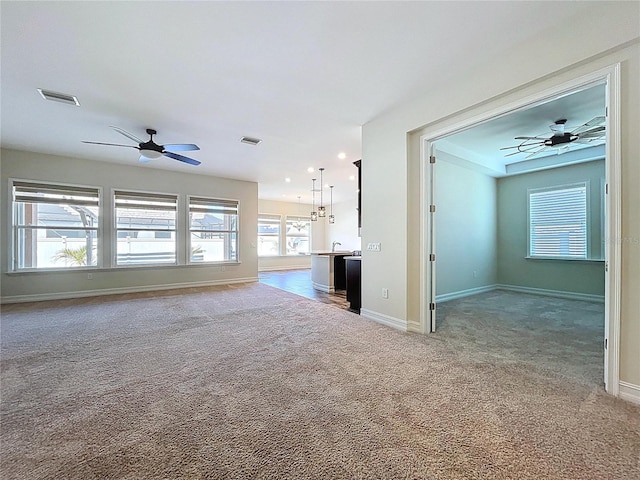 unfurnished living room with visible vents, baseboards, ceiling fan, and light carpet