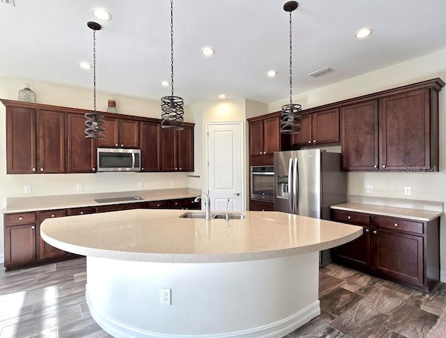 kitchen with a kitchen island with sink, decorative light fixtures, visible vents, a sink, and stainless steel appliances