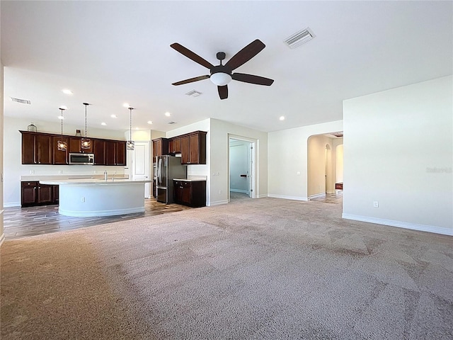 unfurnished living room with ceiling fan, visible vents, and light carpet