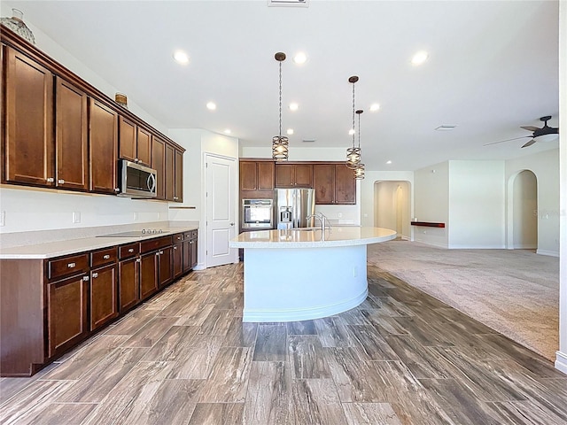 kitchen featuring a kitchen island with sink, decorative light fixtures, arched walkways, light countertops, and stainless steel appliances