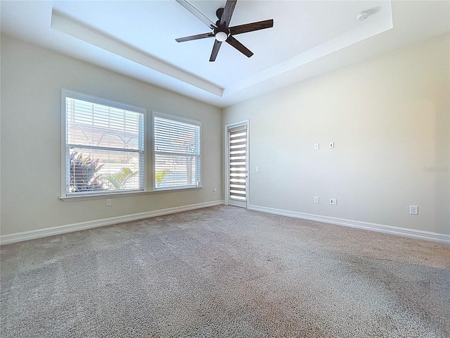 empty room featuring a raised ceiling, ceiling fan, carpet, and baseboards