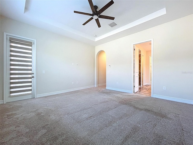 empty room featuring visible vents, carpet floors, ceiling fan, a tray ceiling, and arched walkways