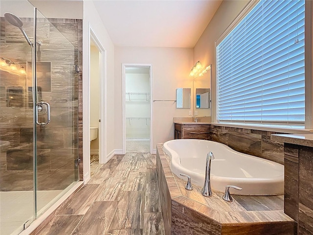 full bathroom with vanity, baseboards, a shower stall, a spacious closet, and a garden tub