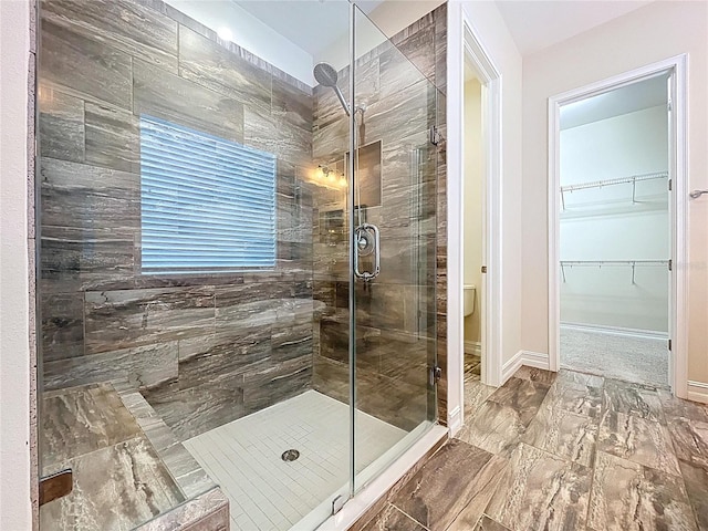 bathroom featuring baseboards, a spacious closet, and a shower stall