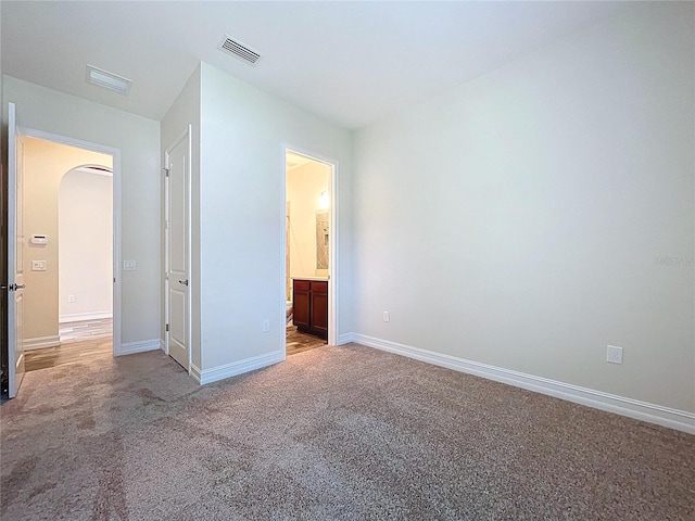 unfurnished bedroom with visible vents, arched walkways, baseboards, and carpet flooring