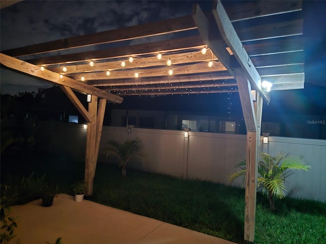 patio at night featuring a pergola and fence