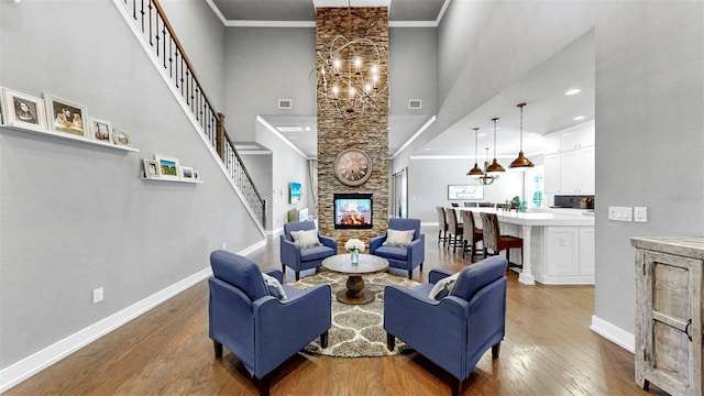 living area with a stone fireplace, a towering ceiling, hardwood / wood-style flooring, baseboards, and a chandelier