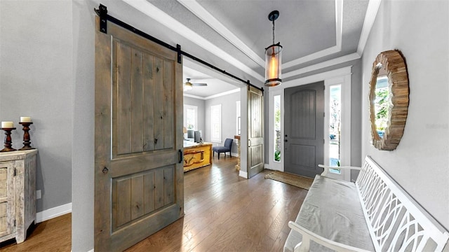 entrance foyer with a barn door, a raised ceiling, a wealth of natural light, and hardwood / wood-style floors