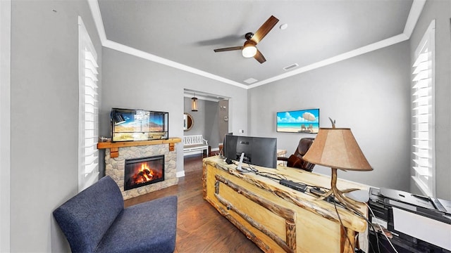 office featuring dark wood-style flooring, ceiling fan, a stone fireplace, visible vents, and ornamental molding