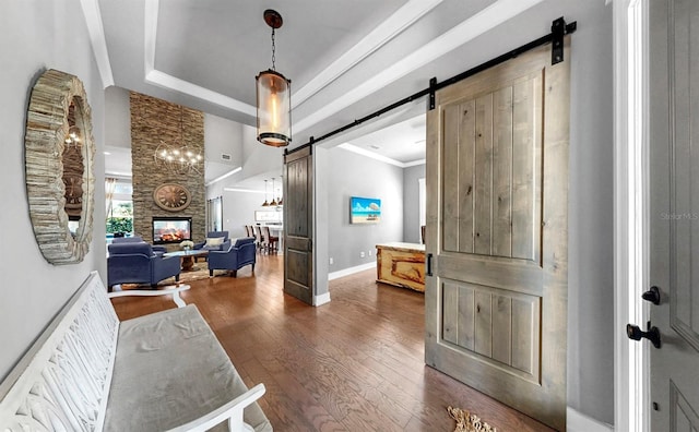 hall featuring crown molding, dark wood-style flooring, a barn door, baseboards, and a tray ceiling
