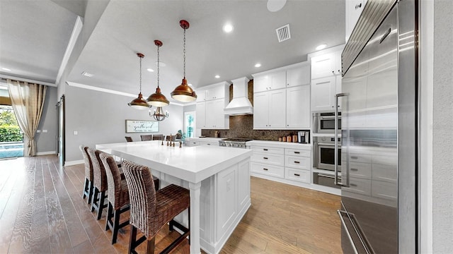 kitchen featuring custom range hood, light wood-style flooring, tasteful backsplash, and stainless steel appliances