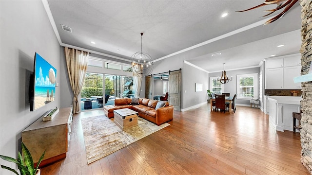 living area with visible vents, ornamental molding, a barn door, a chandelier, and a wealth of natural light