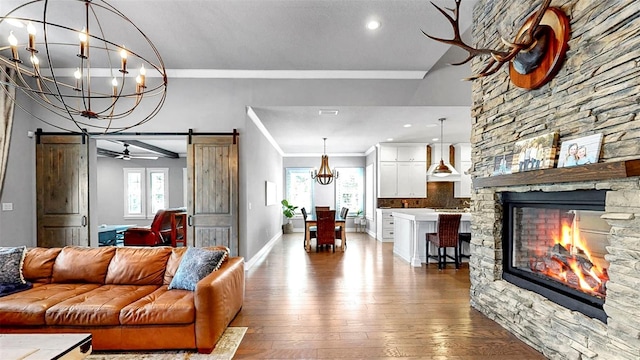 living area featuring plenty of natural light, crown molding, a barn door, wood-type flooring, and an inviting chandelier