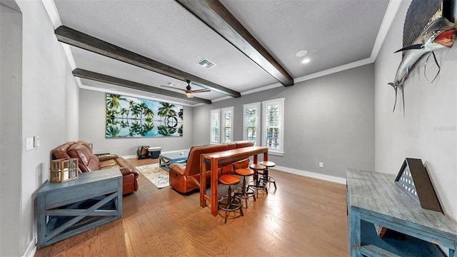 home theater room featuring beam ceiling, a textured ceiling, baseboards, wood finished floors, and visible vents