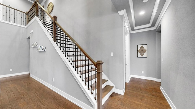 stairs with crown molding, baseboards, wood finished floors, and a high ceiling