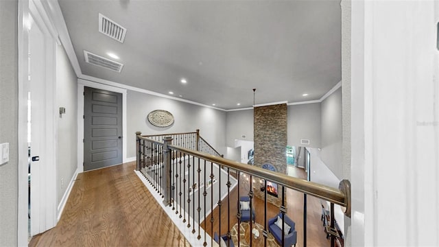 hallway featuring visible vents, ornamental molding, wood finished floors, and an upstairs landing