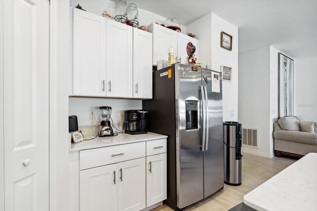 kitchen featuring open floor plan, stainless steel fridge with ice dispenser, white cabinetry, visible vents, and light wood-style floors