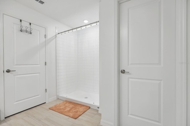 bathroom featuring wood finished floors, visible vents, and a tile shower
