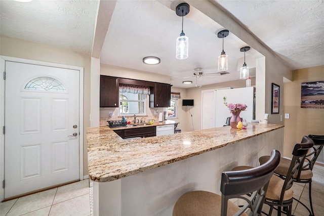 kitchen with a peninsula, dark brown cabinetry, white appliances, a kitchen breakfast bar, and light stone counters