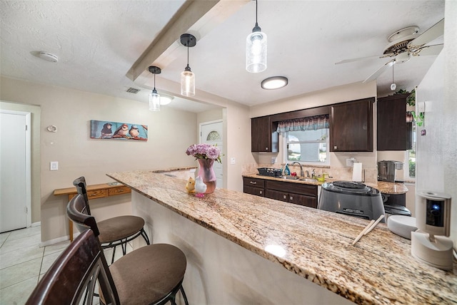 kitchen with a sink, a kitchen breakfast bar, dark brown cabinetry, and decorative light fixtures