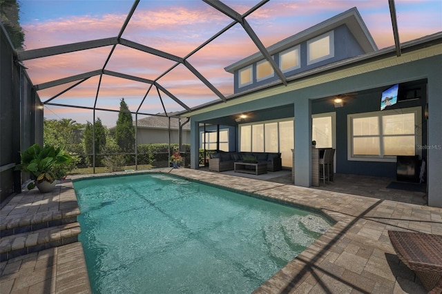 pool at dusk with an outdoor hangout area, glass enclosure, a patio area, and an outdoor pool