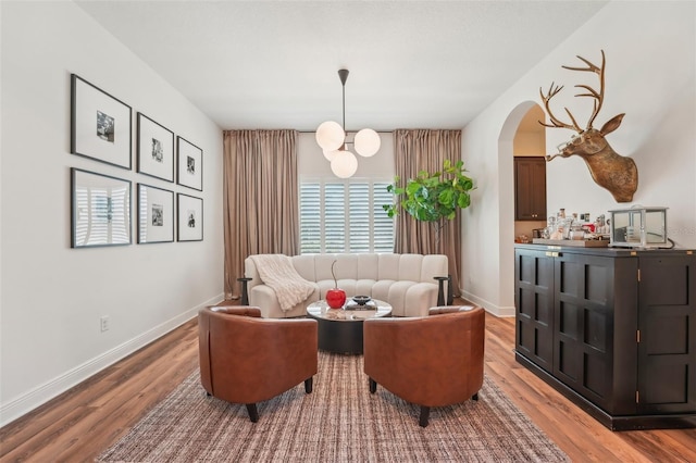 living area featuring arched walkways, baseboards, and wood finished floors