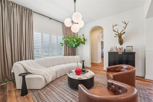 living area with baseboards, arched walkways, and wood finished floors