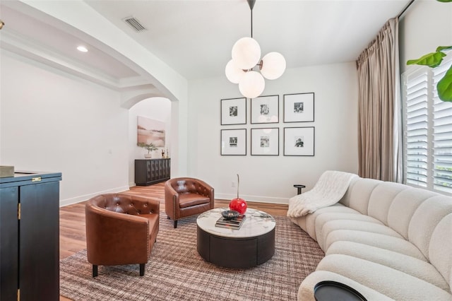 living room featuring arched walkways, baseboards, wood finished floors, and visible vents